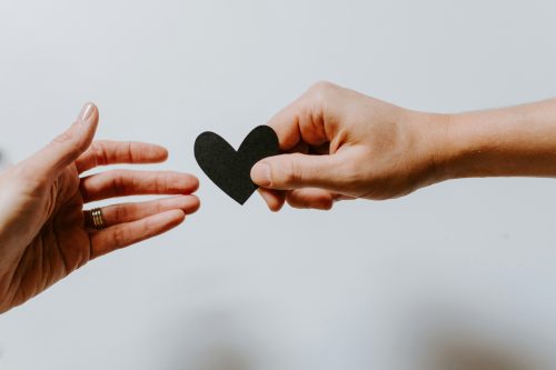 one hand passing a cut-out paper heart to another hand symbolizing support