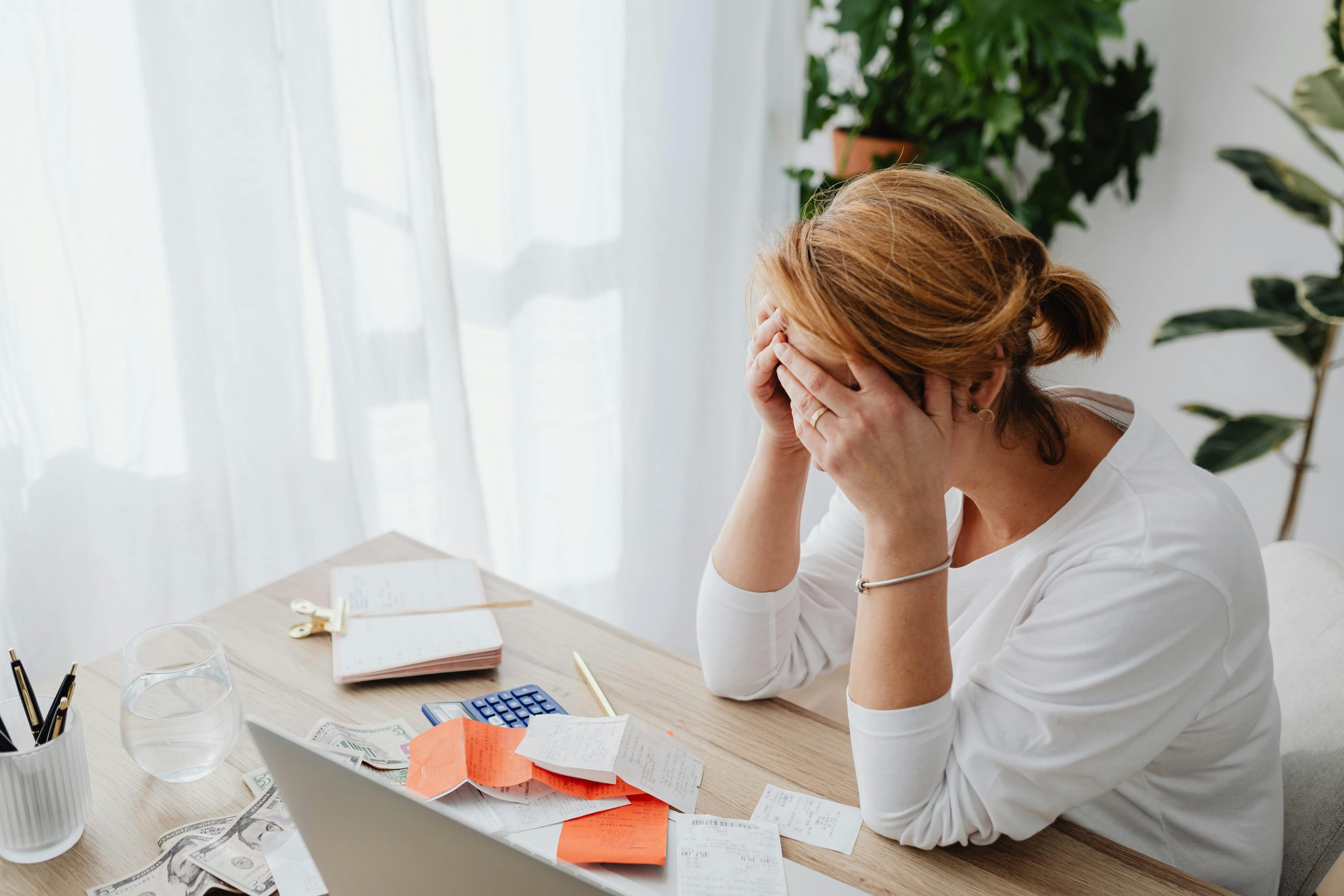 woman holding her head in her hands with financial documents on a desk.