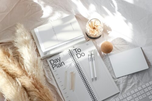 pens lying on notebooks to be used to compile a founder mental health plan laid on a white desk with a candle beside them